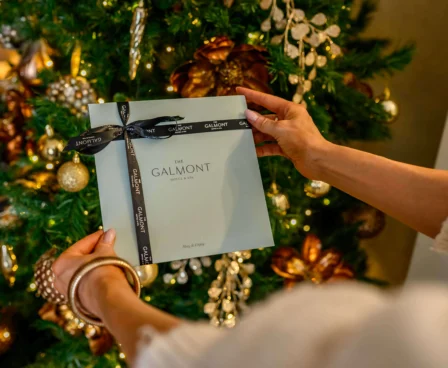 Person holding a Galmont gift box by a festive Christmas tree.