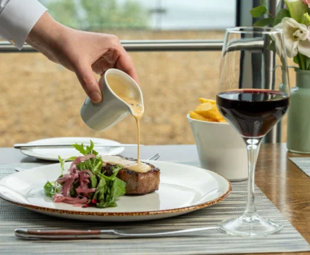 Elegant dining with steak, garden salad, and red wine by the sea.