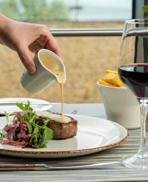 Elegant dining with steak, garden salad, and red wine by the sea.