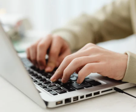 Hands typing on a laptop, engaging in online activity.