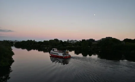 A family enjoys a serene evening river cruise under a twilight sky near lush greenery.