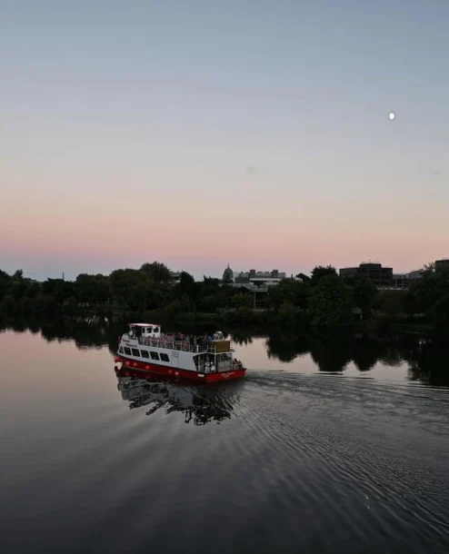 A family enjoys a serene evening river cruise under a twilight sky near lush greenery.